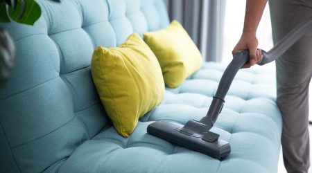 close up of man's hand cleaning couch using vacuum cleaner at home