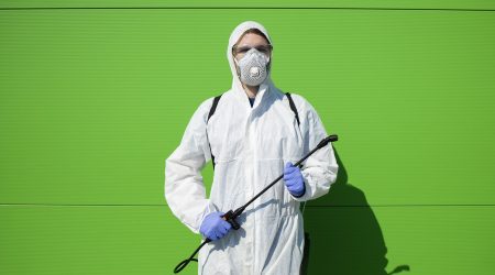 Portrait of person in chemical protection suit holding sprayer for disinfection to stop spreading corona virus.